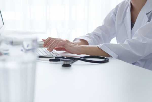 Doctor in a white lab coat is seated and typing at a computer